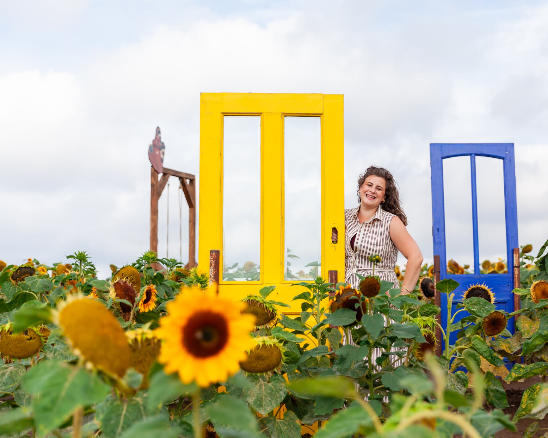 Kate Keir laughing beside a bright yellow door in a sunflower field