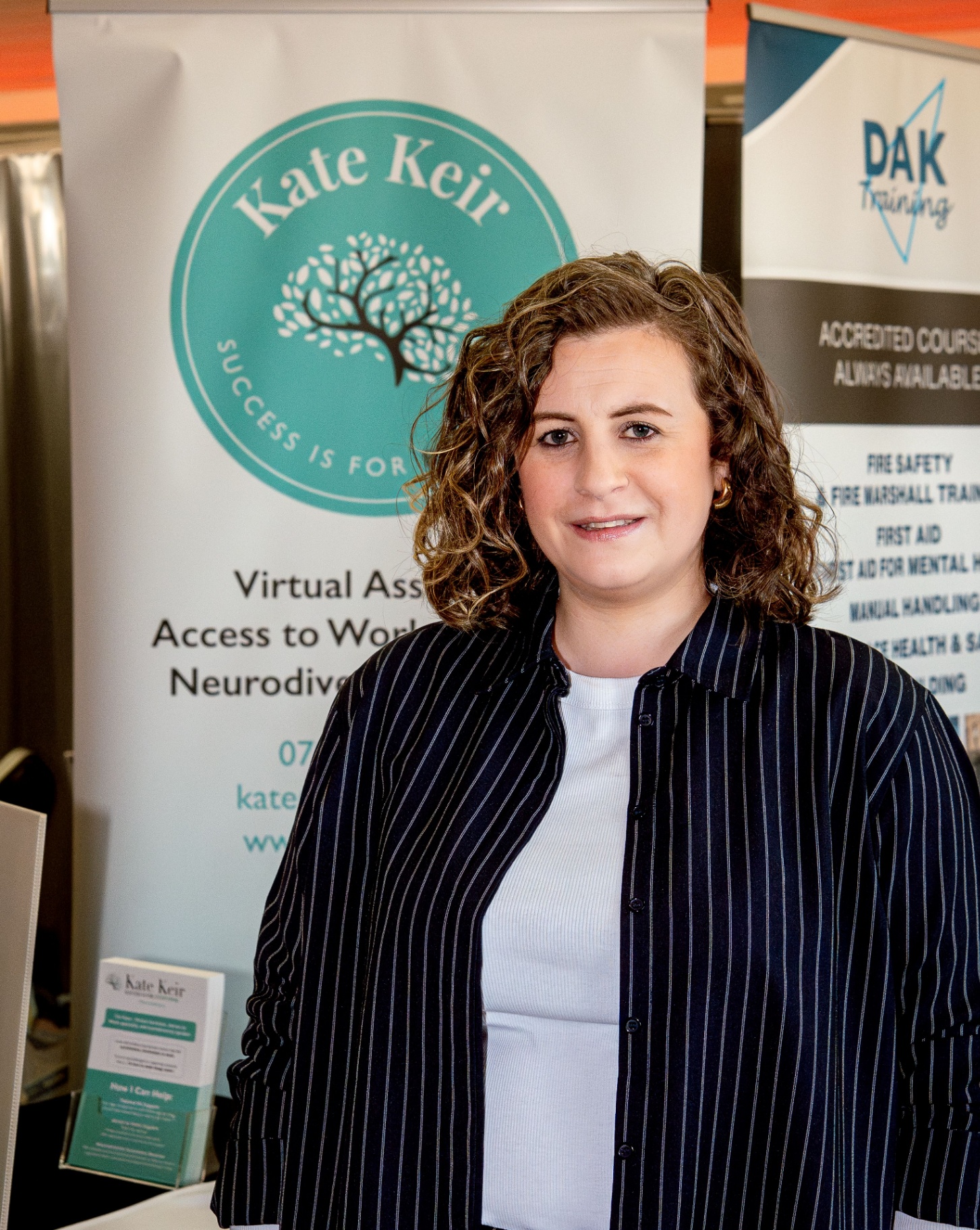 Kate Keir standing beside her branded Kate Keir banner at an event.